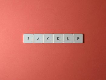 Free Close-up of keyboard keys spelling 'BACKUP' placed on a coral-colored surface. Stock Photo