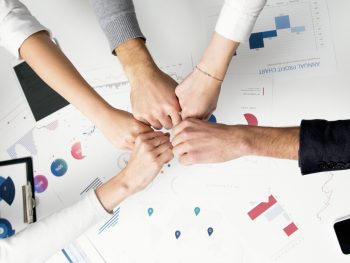 Free Colleagues celebrate success with a fist bump over financial charts depicting teamwork and unity. Stock Photo
