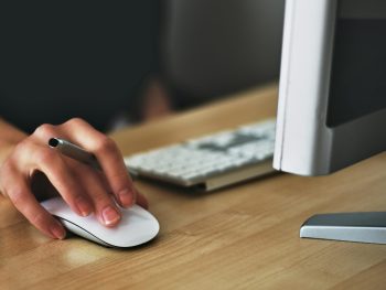 Free A hand using a wireless mouse at a modern desk setup with a computer and keyboard. Stock Photo